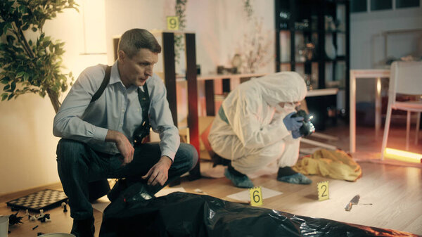 The detective is examining the crime scene and working with the forensic expert on a homicide case