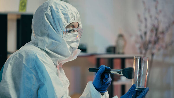 A forensic lab expert is dusting glass for fingerprints and collecting crime evidence