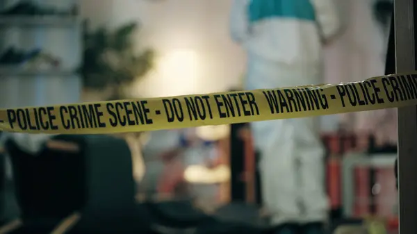 Adli tıp uzmanları odayı inceliyor ve olay yeri bandının arkasında kanıt topluyorlar.