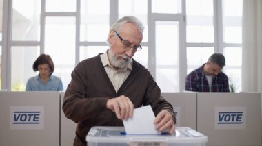 Üst düzey bir adam oy kullanma merkezindeki sandığa oy veriyor. Vatandaşların oy vermelerine aktif olarak katılıyor.