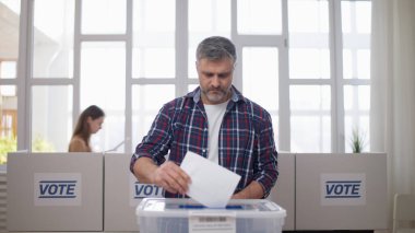 Orta yaşlı bir adam sandık merkezinde oy veriyor, seçim günü sandığa oy atıyor.