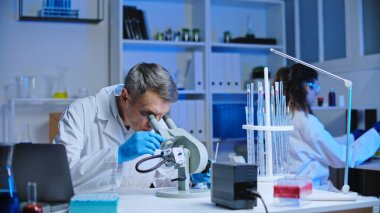 Kimya laboratuvarı bilim adamı maddeyi mikroskop altında inceliyor, araştırma yapıyor.