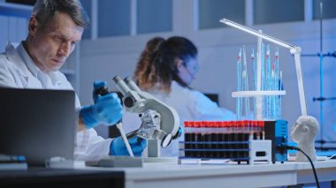 Laboratuvar teknisyeni mikroskop altında kan örneği ve sağlık kontrolü yapıyor.