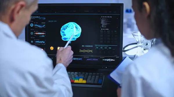 Senior scientist drawing intern\'s attention to 3D brain image, working in neurology diagnostics lab