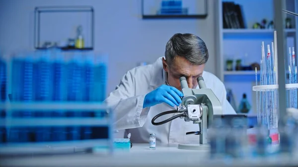 Laboratory scientist studying material under microscope, vaccine development