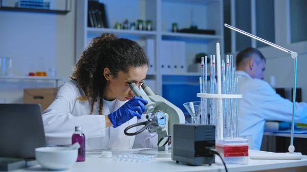 Female laboratory worker examining cosmetic sample under microscope, science