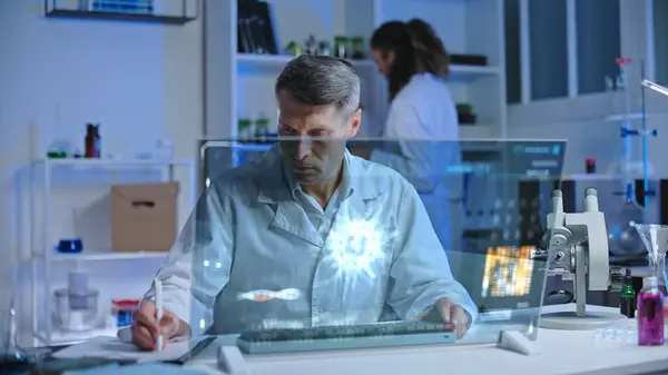 Lab scientist looking at virus hologram on computer screen, writing down test data