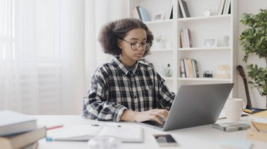 Gözlüklü siyahi kız dizüstü bilgisayarda, internette, okulda proje yapıyor.