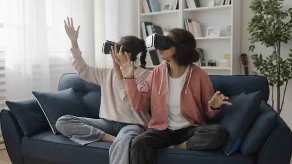 Young sisters feeling amazed, experiencing virtual reality in vr headsets, modern technology