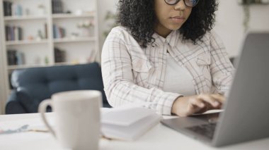 Yarı zamanlı bir işte çalışan Afro-Amerikalı bir kadın, bilgisayarında evden bağımsız olarak çalışıyor.