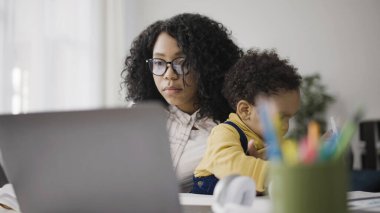 Anne dizüstü bilgisayar, ek gelir ve annelik izni üzerinde çalışırken, bebek kalemle oynuyor.