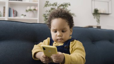 Merak uyandıran Afrikalı Amerikalı bebek ailesinin akıllı telefonuyla oynuyor, patronluk taslıyor.