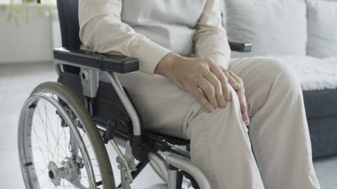 Engelli bir adam yaralı bir bacağa masaj yapıyor, tekerlekli sandalyede oturuyor, rehabilitasyon merkezinde.