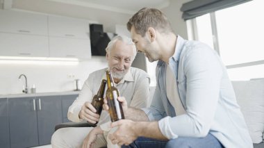 Mutlu kıdemli baba ve küçük oğul bira şişelerini tokuşturup gülümsüyor, kutluyor.
