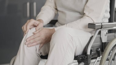 Tekerlekli sandalyede oturan yaralı adam, yaralı diz masajı, fiziksel rehabilitasyon.