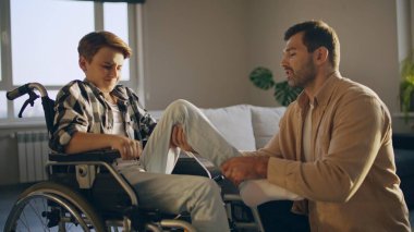 Baba engelli oğluna tekerlekli sandalyede rehabilitasyon ve aile bakımında yardım ediyor.