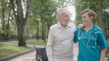 Bakıcı hemşire kıdemli adamı destekliyor ve ona yürüme ve rehabilitasyon konusunda yardım ediyor.