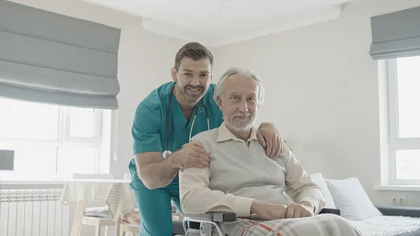 Portrait of smiling nurse and happy elderly man in wheelchair in a retirement home, patient care