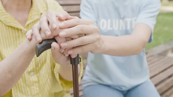 Senior companion supporting woman with a walking stick, holding hands, care