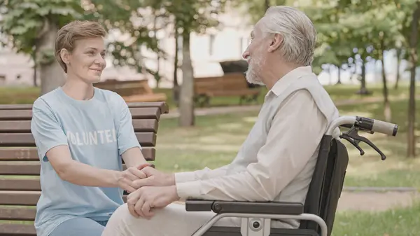 Elderly care volunteer talking to senior man in wheelchair, psychological support