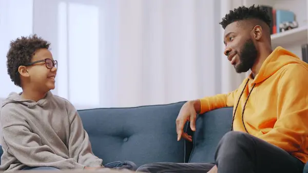 stock image African American father and little son having conversation on couch, spending time together