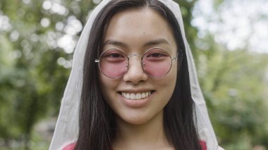 Pembe gözlüklü mutlu Asyalı kadın kameraya gülümsüyor, tasasız kadın portresi.