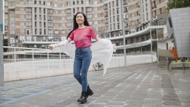 Beyaz yağmurluklu güzel Asyalı kız öğrenci sokakta dans ediyor, kutlama yapıyor.