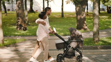 Genç adam karısını kucaklıyor, dışarıda bebek arabasıyla yürüyor, mutlu ebeveynler, sevgi
