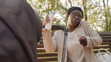 Çalışan bir anne bebek arabasında bebek maması yiyor ve telefonla konuşuyor.