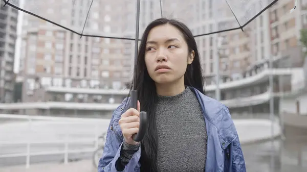 Üzgün Asyalı kadın şemsiyeyle yağmurlu sokakta yürüyor, hayal kırıklığı, mahvolmuş planlar.