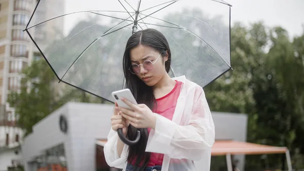 Female scrolling app on smartphone, ordering taxi or shopping online in rainy weather