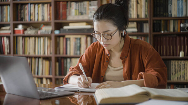 Tired young woman studying in a library, overburdened with work, academic pressure