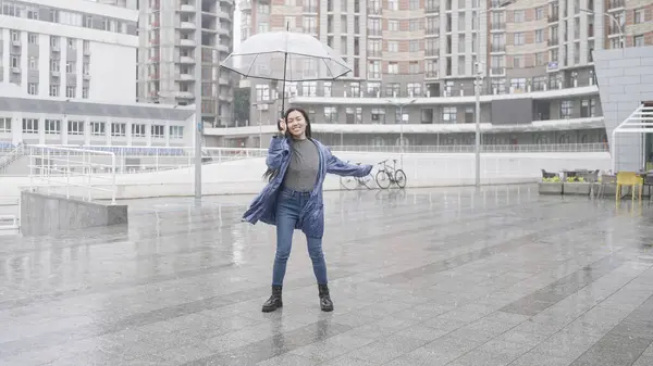 Young happy woman dancing in the rain under umbrella, walking in city, positive mood