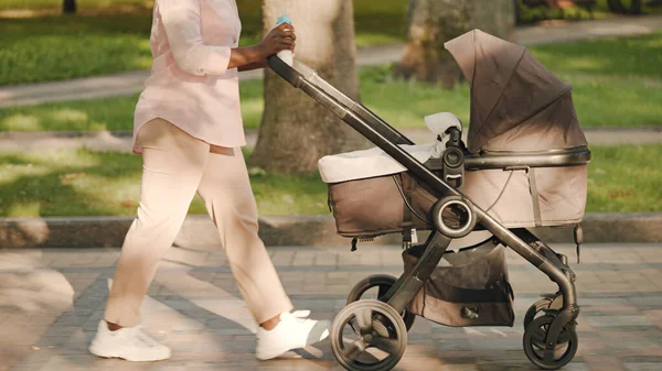 Modern mom in casual clothes pushing pram, walking in park with infant, family
