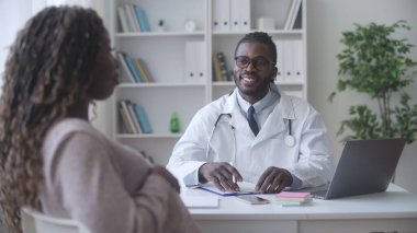 Gülümseyen doktor kadın doğum uzmanı hamile zenci kadının sağlık kontrollerini yapıyor.