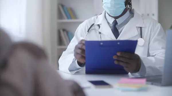Doctor in face mask filling medical form, listening to pregnant woman complaints