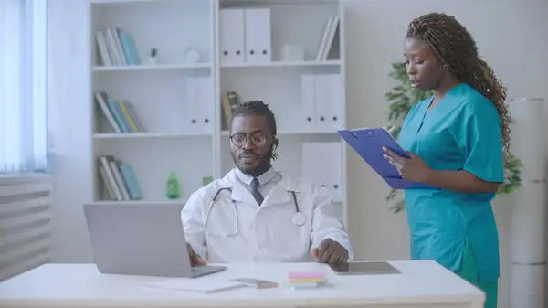 African nurse talking with male doctor, filling forms, colleagues at workplace