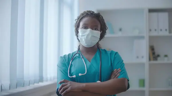 Professional female doctor in face mask crossing hands, work during pandemic