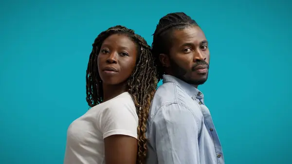 Black couple standing back to back on blue background, people of color community