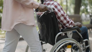 Park boyunca engelli bir adamın tekerlekli sandalyesini iten kadın, dışarıda yürümek, rehabilitasyon
