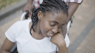 Tekerlekli sandalyedeki kadını destekleyen Afro-Amerikalı bir adam.