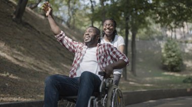 Parkta heyecanlı erkek arkadaşı olan tekerlekli sandalyeyi iten mutlu genç kadın iyileşiyor.