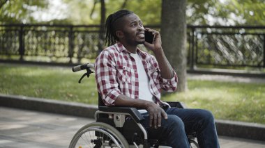 Engelli yakışıklı Afro-Amerikan adam tekerlekli sandalyede oturuyor ve telefonda konuşuyor, gülümsüyor.
