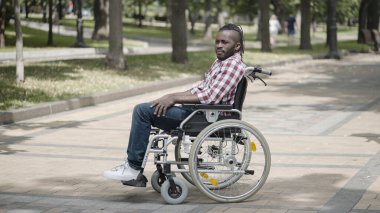 Parkta tekerlekli sandalyede tek başına oturan özürlü Afrikalı Amerikalı bir adam.