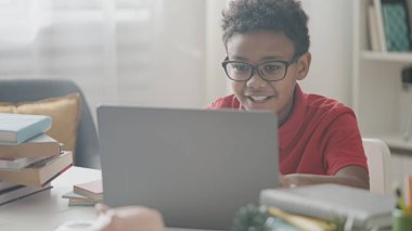 Gözlüklü zeki siyah çocuk laptopta ödev yapıyor çalışırken eğleniyor.