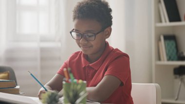 Gözlüklü meraklı öğrenci kitap okuyor, ödev yazıyor, ders çalışıyor.