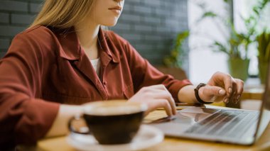 Kafede çalışan, dizüstü bilgisayar kullanan, kahve içen ciddi genç bir kadın.