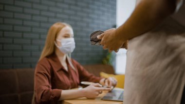 Yüz maskeli kadın restoranda, salgın güvenliği için temas kurmadan ödeme yapıyor.