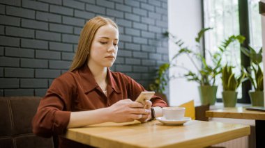 Genç sarışın kadın kahve dükkanında akıllı telefon uygulaması kullanıyor, mobil alışveriş yapıyor, taksi çağırıyor.