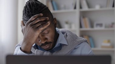 Afrikalı Amerikalı bir adam bilgisayarla uzun saatler çalıştıktan sonra yorgun ve baş ağrısı çekiyor.